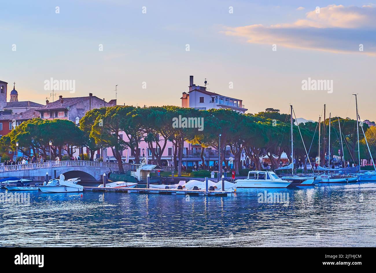 The tall spread pines along the bank of Lake Garda with yachts in port, Desenzano del Garda, Lombardy, Italy Stock Photo