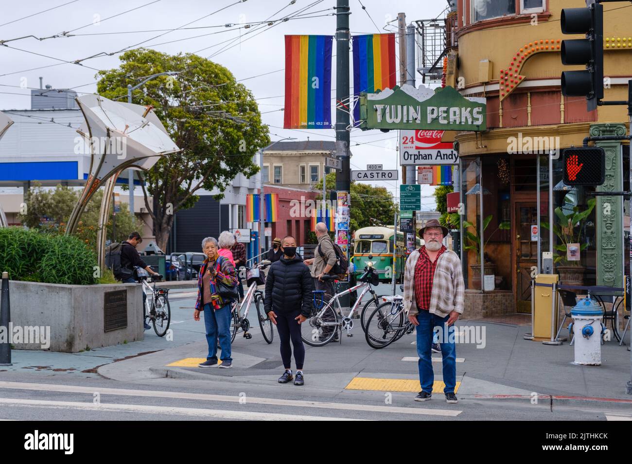 People cross the street at Castro & 17th, in front of Twin Peaks Tavern, with The Seed sidewalk plaque, tall LED flowers. by Aphidoidea on the left. Stock Photo
