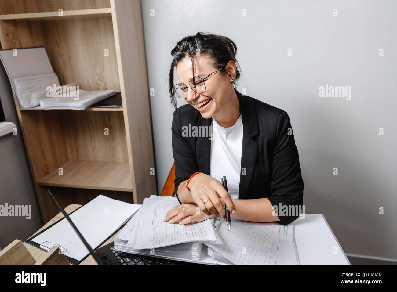 A smiling woman sitting at her desk in the office. A happy businesswoman sitting in her office. Worker in the office in a good mood. Stock Photo