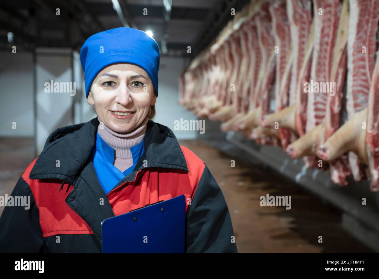 Meatpacking plant worker in front of butchered carcasses. Meat