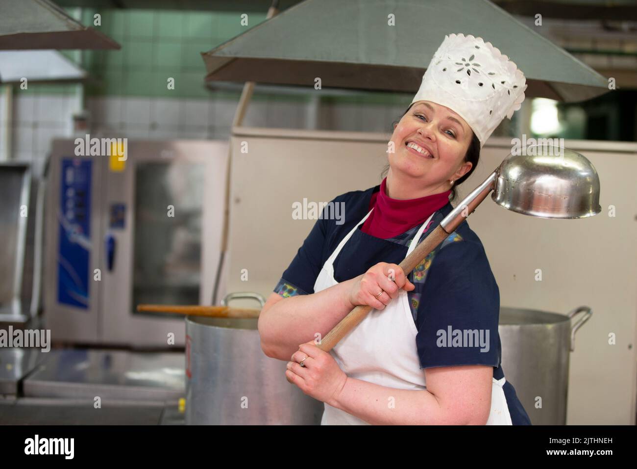 A chef with a large ladle poses in front of an industrial kitchen and ...