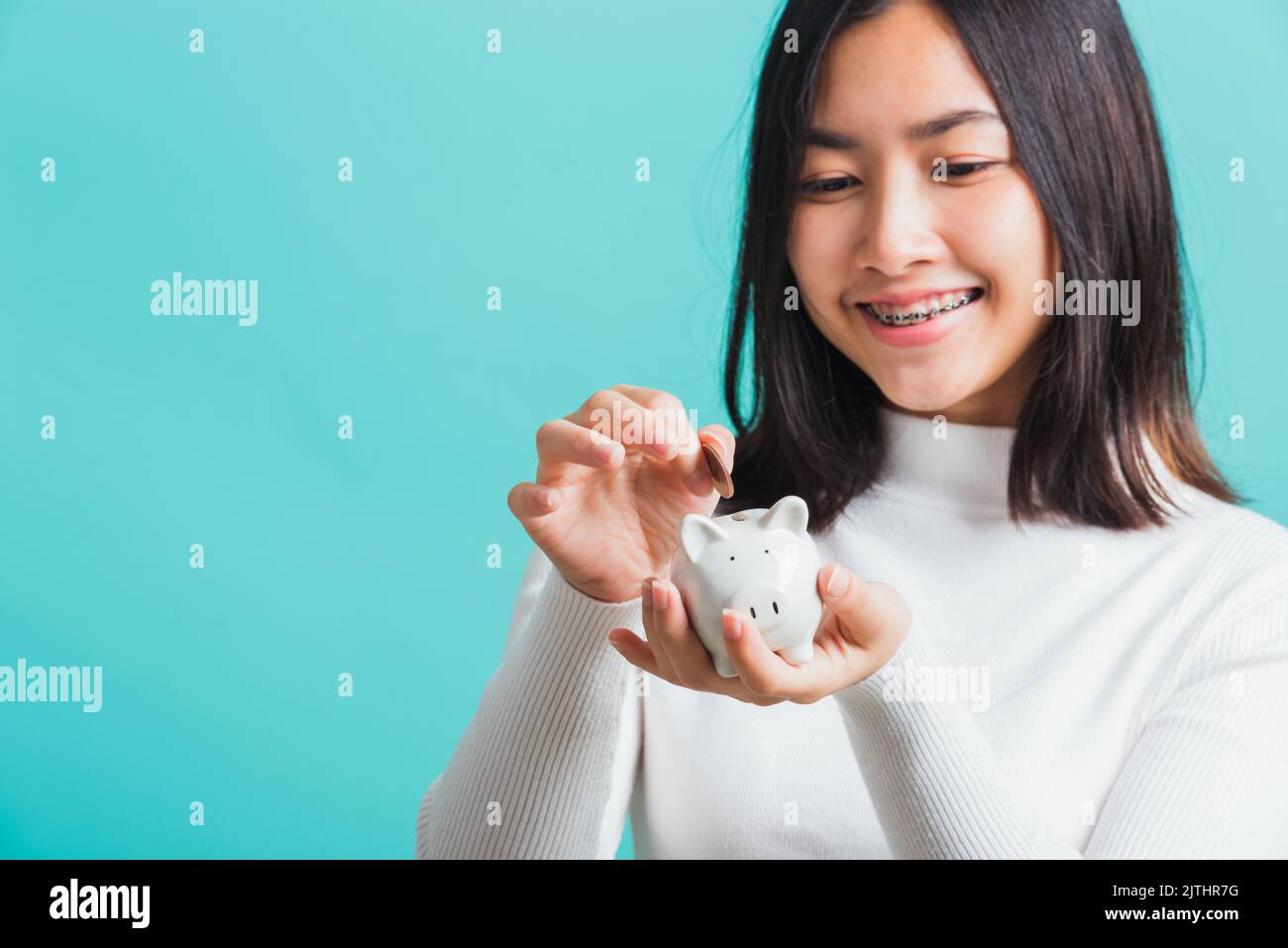 Asian beautiful young woman holding piggy bank on hands and putting ...