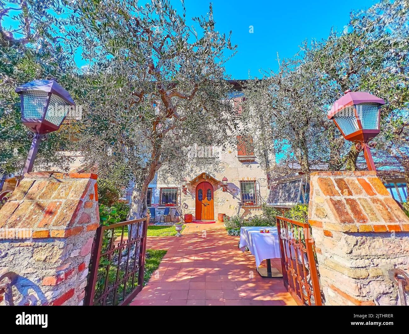 The cozy rustic style outdoor restaurant in a shady olive orchard in front of historic house, Sirmione, Italy Stock Photo
