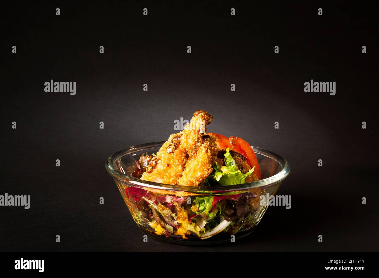 Green salad with chicken fingers on top in a big bowl over a black background Stock Photo