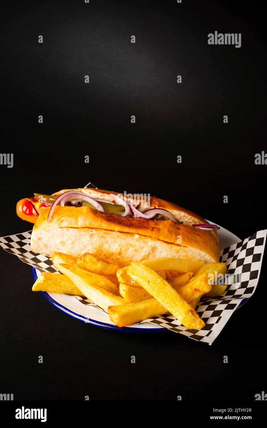 Frankfurt sausage with onion accompanied with french fries on a white plate over a black background Stock Photo