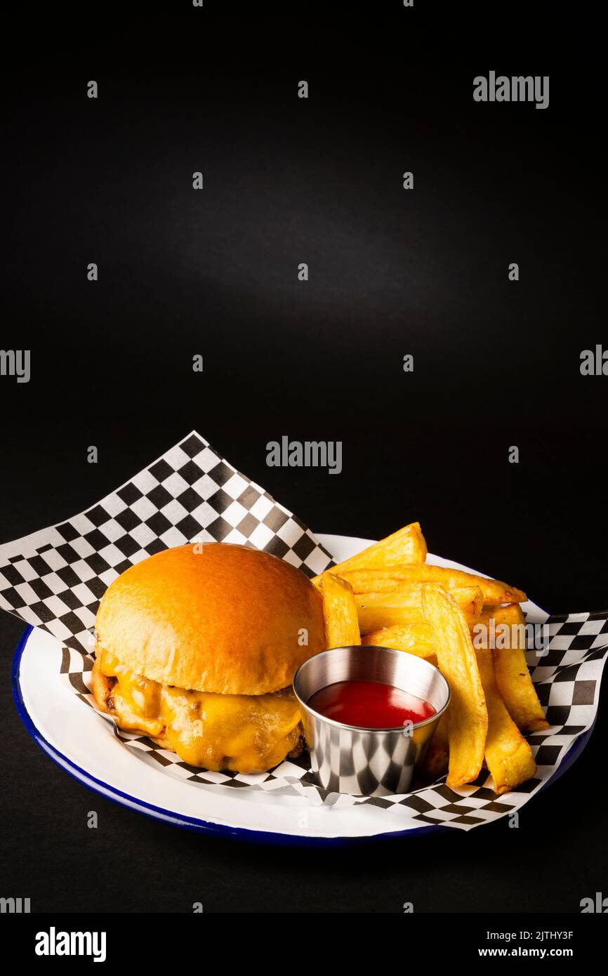 Two smashed hamburgers with cheese accompanied with french fries on a white plate over a black background Stock Photo