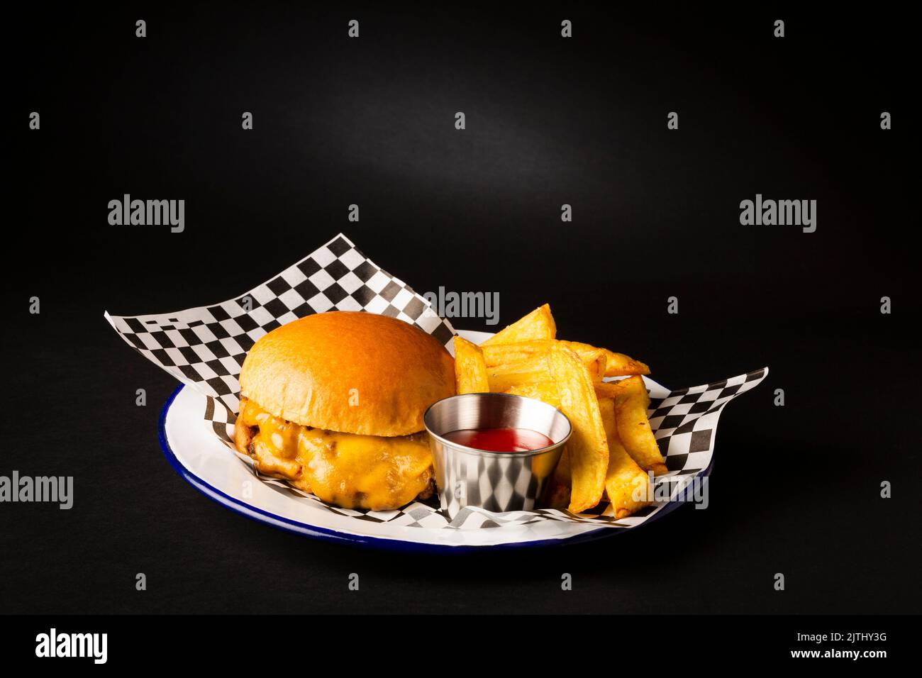 Two smashed hamburgers with cheese accompanied with french fries on a white plate over a black background Stock Photo