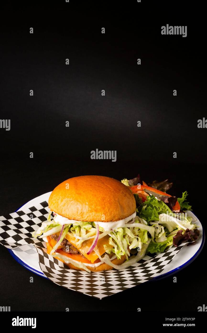 Two smashed hamburgers with cheese accompanied with a green salad on a white plate over a black background Stock Photo