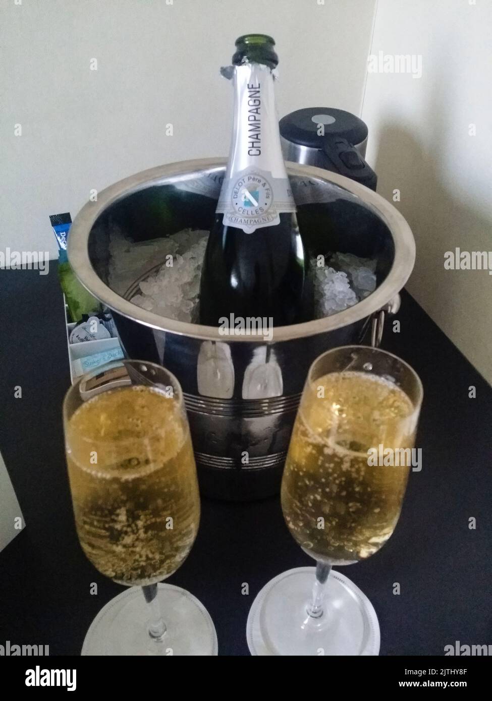 Bottle of champagne in a bucket of ice with champagne glasses in a hotel room. Stock Photo