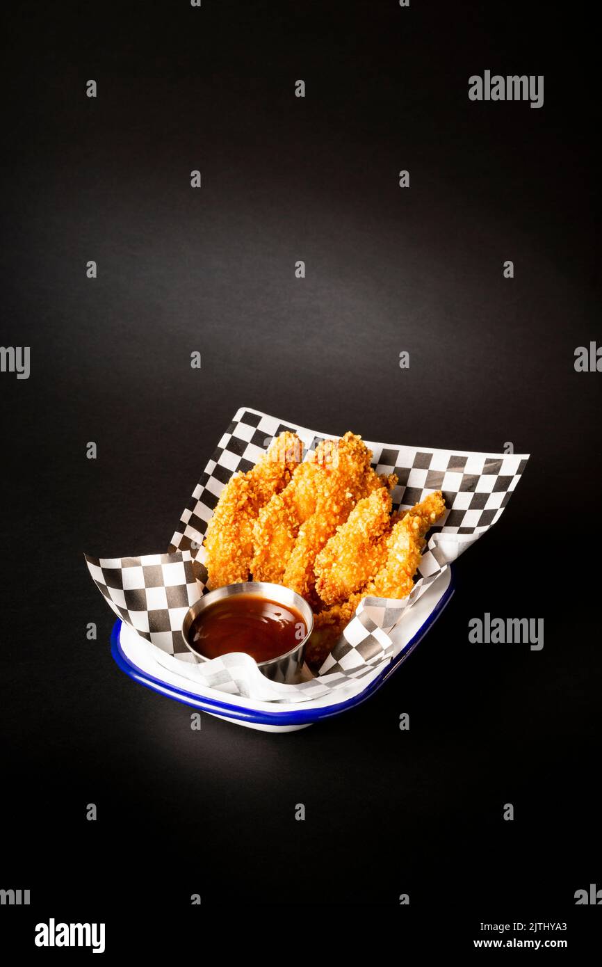Chicken fingers with ketchup sauce on a plate over a black background Stock Photo