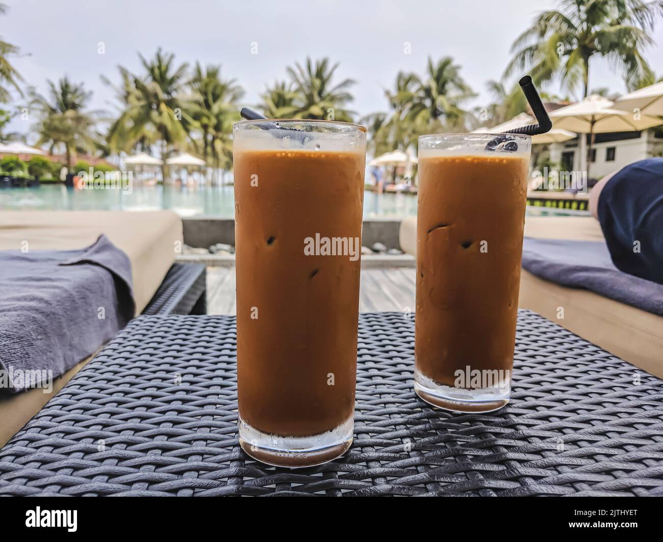 Two glasses of Vietnamese coffee, strong coffee with condensed milk and ice at a hotel swimming pool. Stock Photo