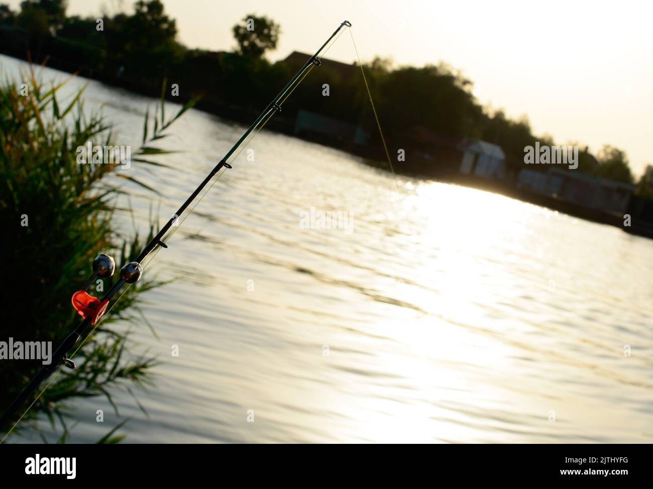 Fishing rod with a red bell on a sunset against river. Stock Photo
