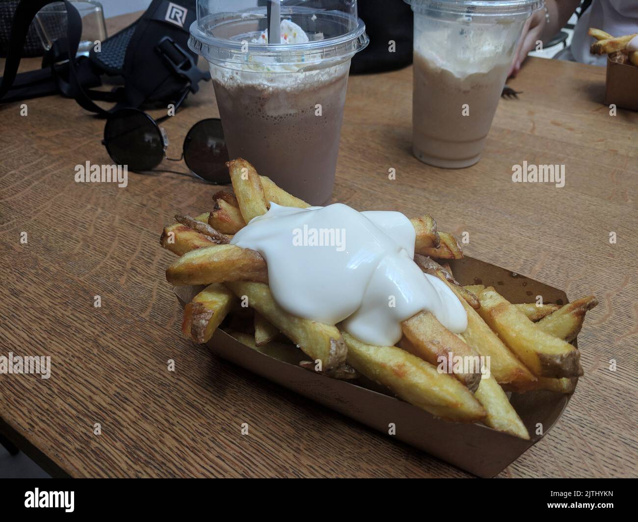 Cardboard box containing chips (french fries) covered in mayonnaise with iced coffee and whipped cream on a table outside a restaurant in The Hague, Netherlands Stock Photo