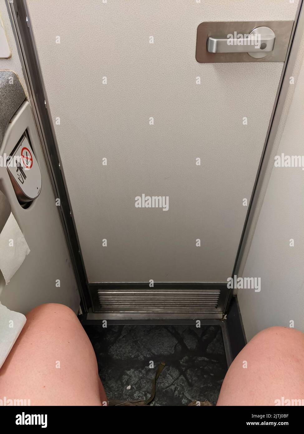 A man sits in a cramped airplane toilet with his knees showing. Stock Photo
