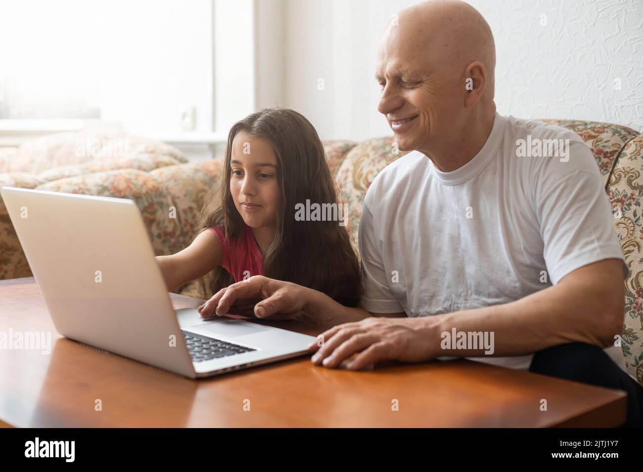 Grandfather and granddaughter spend time together use laptop, browse
