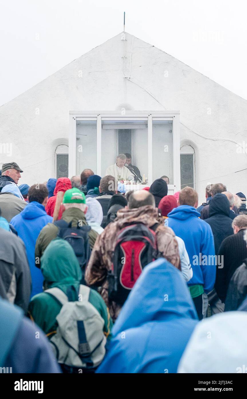 A priest says mass from inside a shelter, while pilgrims form a congregation outside in heavy rain during the Reek Sunday annual pilgramage, Croagh Patrick, County Mayo, Republic of Ireland. Stock Photo