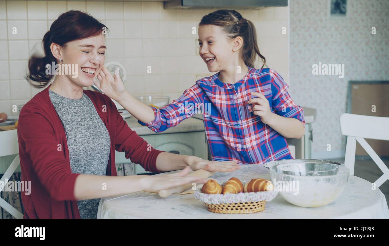 Young mother and her cute daughter have fun smearing nose each other with flour while cooking together in the kitchen on holidays. Family, food, home and people concept Stock Photo