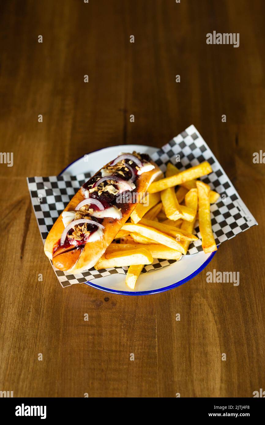 Frankfurt sausage with onion, cheese accompanied with french fries on a white plate on a wooden table Stock Photo