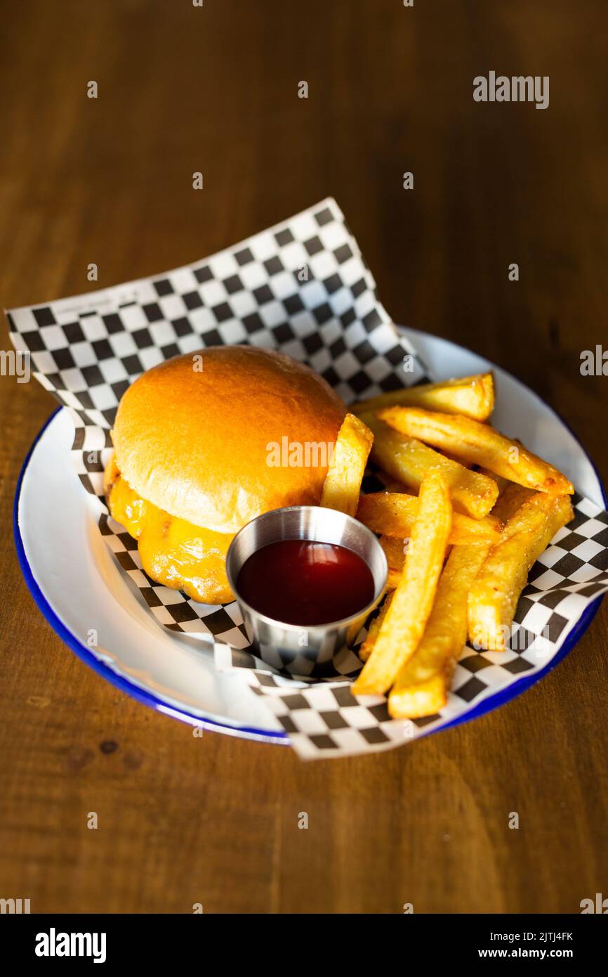 Doble cheese burger accompanied with french fries on a white plate on a wooden table Stock Photo