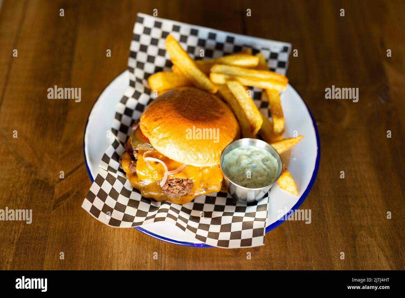 Doble cheese burger with onion accompanied with french fries on a white plate on a wooden table Stock Photo
