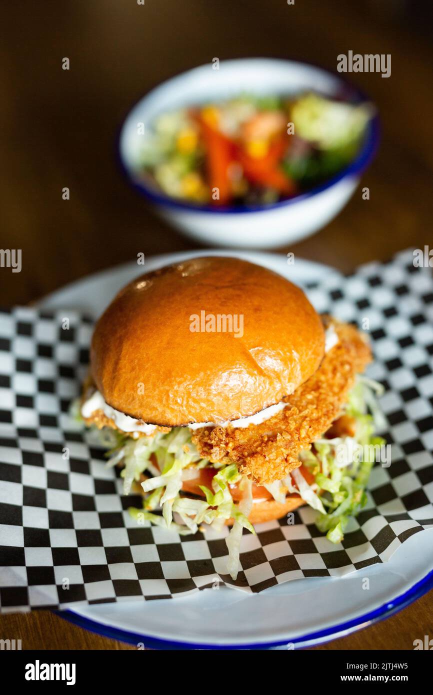 Finger Chicken burger with cheese accompanied with green salad on a white plate on a wooden table Stock Photo