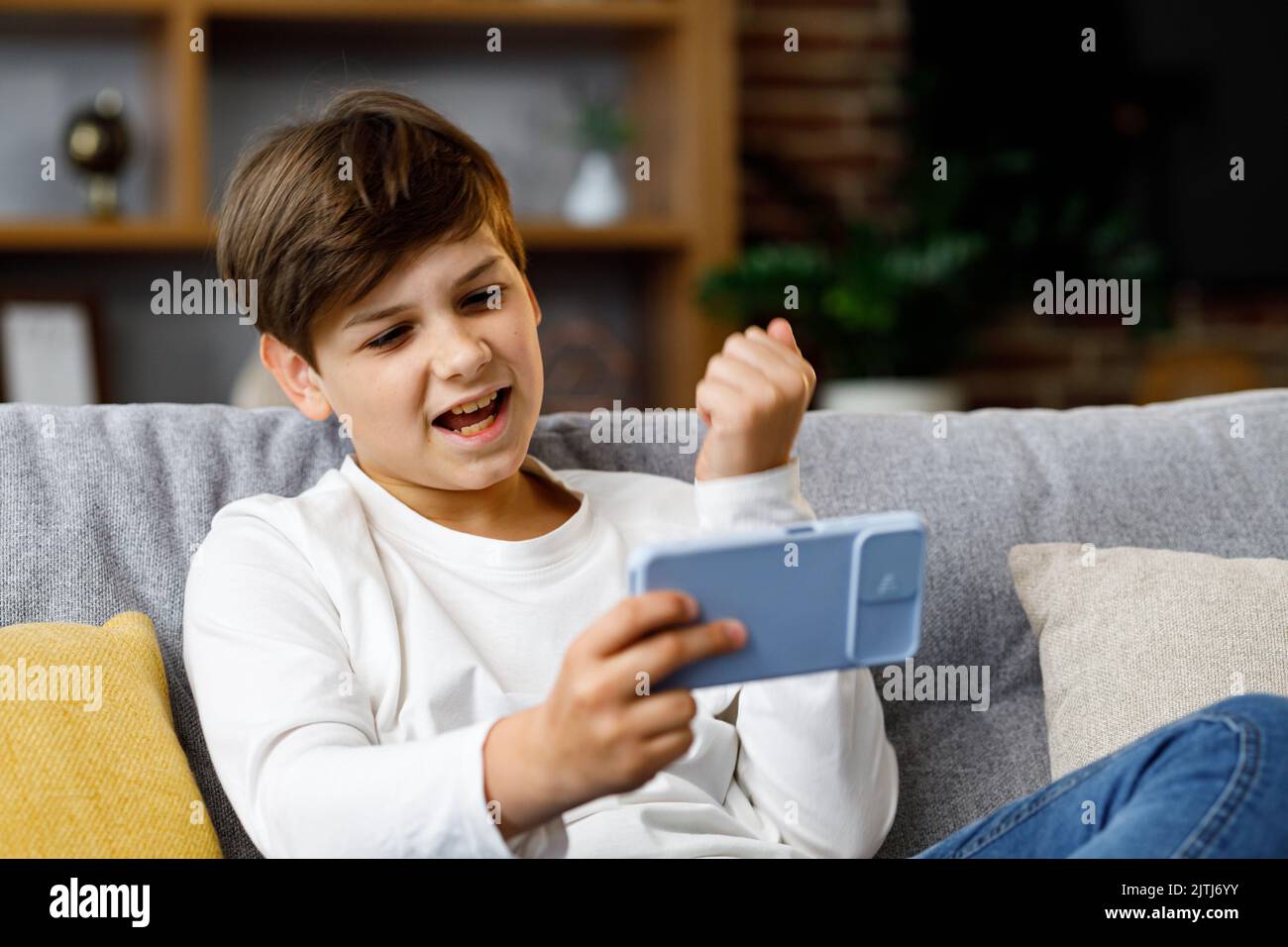 Teens and gaming addiction. Young boy playing video game on smartphone sitting on sofa at home. Cute teenager losing in car racing game on mobile Stock Photo