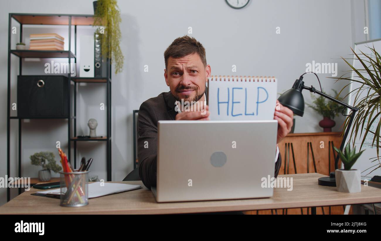 Hopeless sad businessman in formal wear suit working on laptop computer, showing inscription note text Help. Overworked tired freelance business man indoors at office. Poverty, bankrupt, deadline Stock Photo