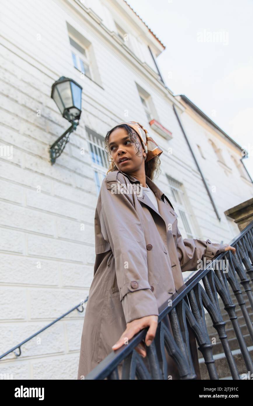 Woman Using Handrail african american woman in headscarf and trendy trench coat touching ...