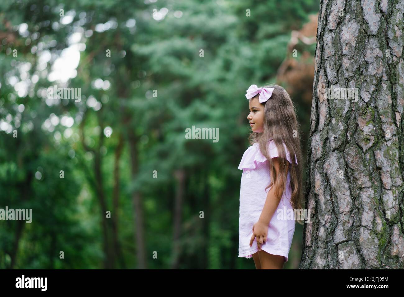 Beautiful girl in a pink dress stands near a tree in the forest and dreams Stock Photo