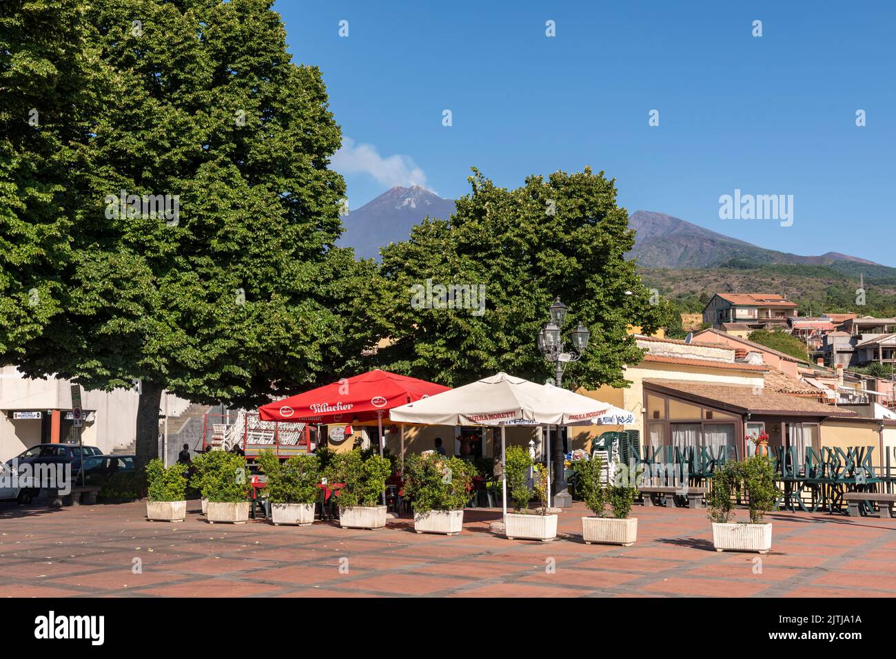 The piazza in the village of Milo, Sicily, with a view of the smoking summit of Mount Etna. Milo is at about 850m on the eastern slope of the volcano Stock Photo