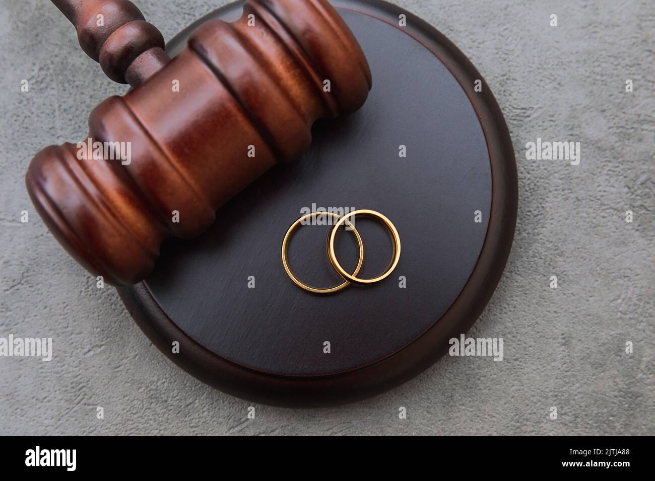 Law theme. Judge gavel wedding rings on concrete stone grey background
