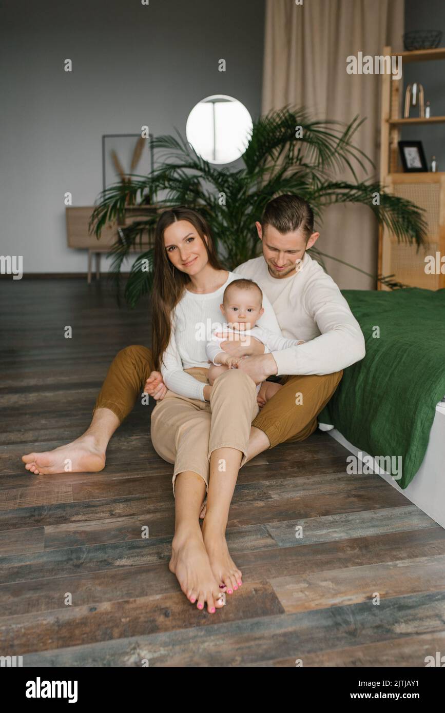 Stylish young family with a baby are sitting on the bedroom floor and enjoying happy moments Stock Photo