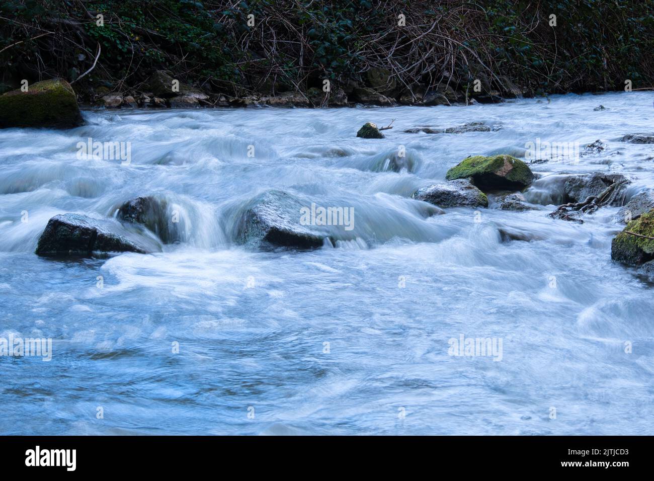 The green angle-covered rocks in fast flowing river, long exposure ...