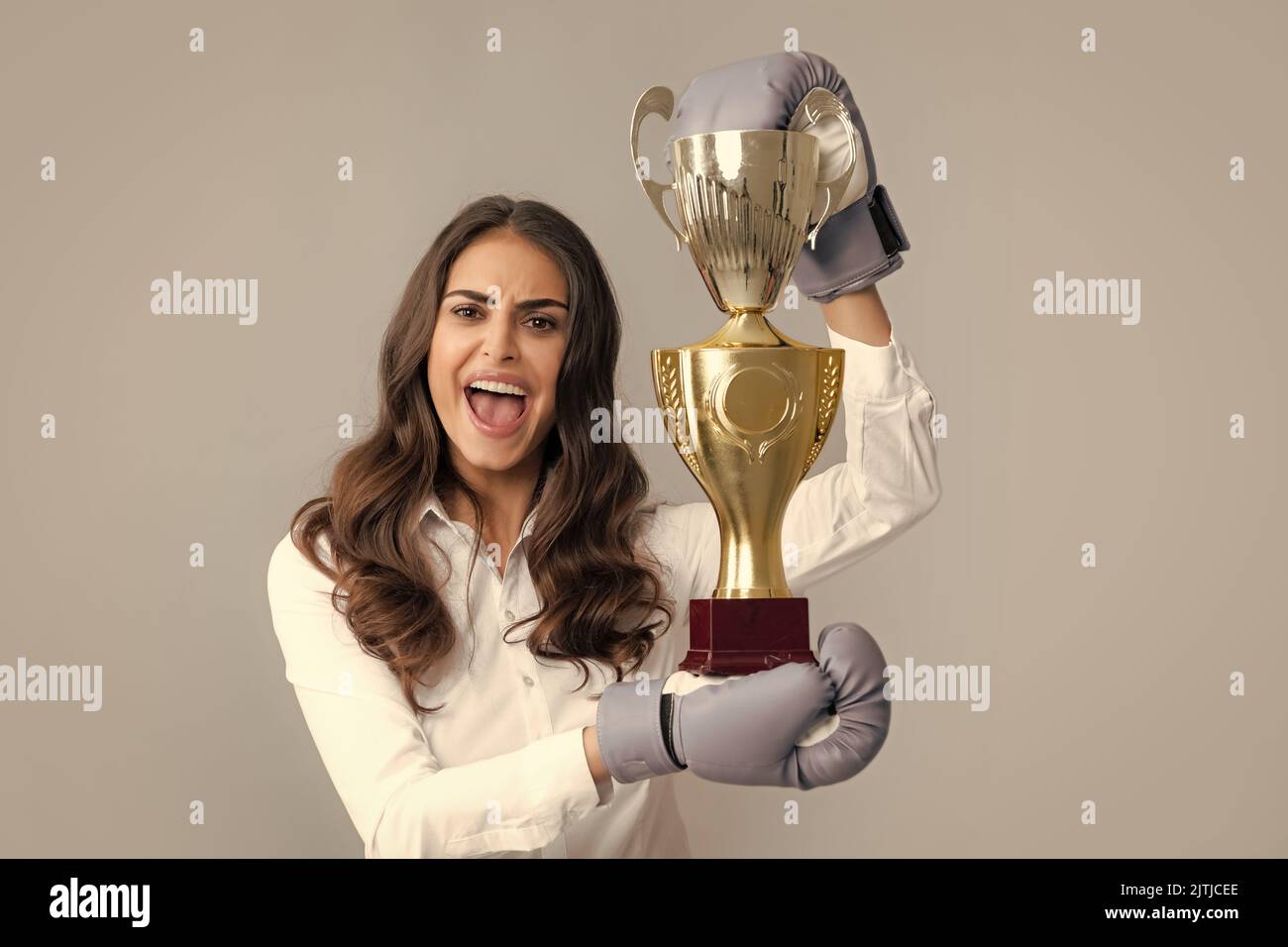 Woman in boxing gloves hold champion winner cup, trophy. Screaming strong young woman boxer. Strong aggressive business woman concept. Winner female Stock Photo