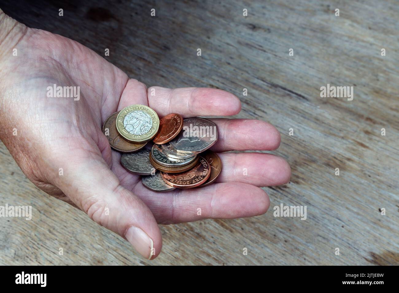 An elderly hand hold a few pounds worth of British coinage. How far