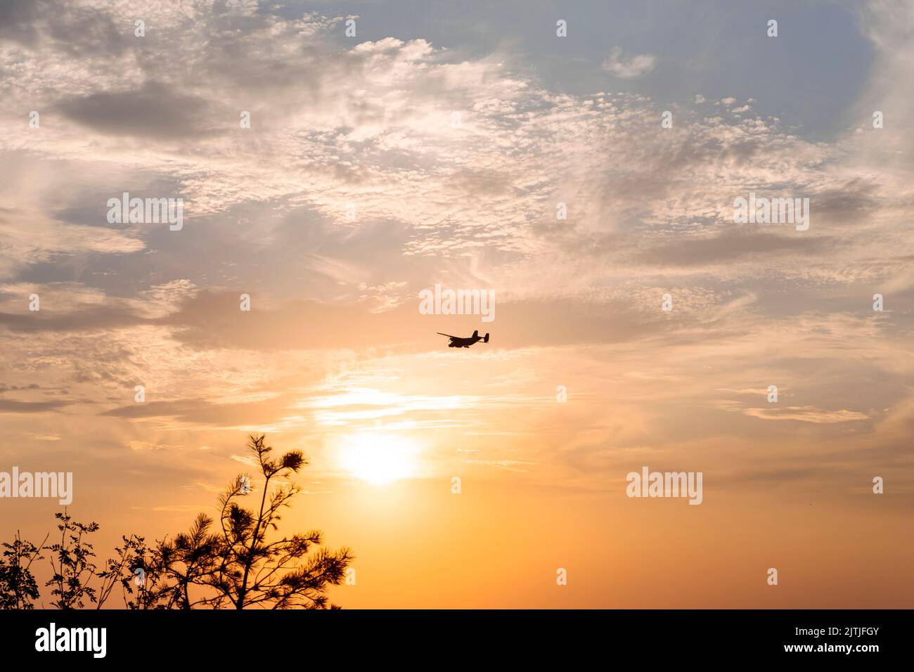 Airplane dark silhouette on orange sunset sky with clouds. Propeller plane outline shape on setting sun background. Stock Photo