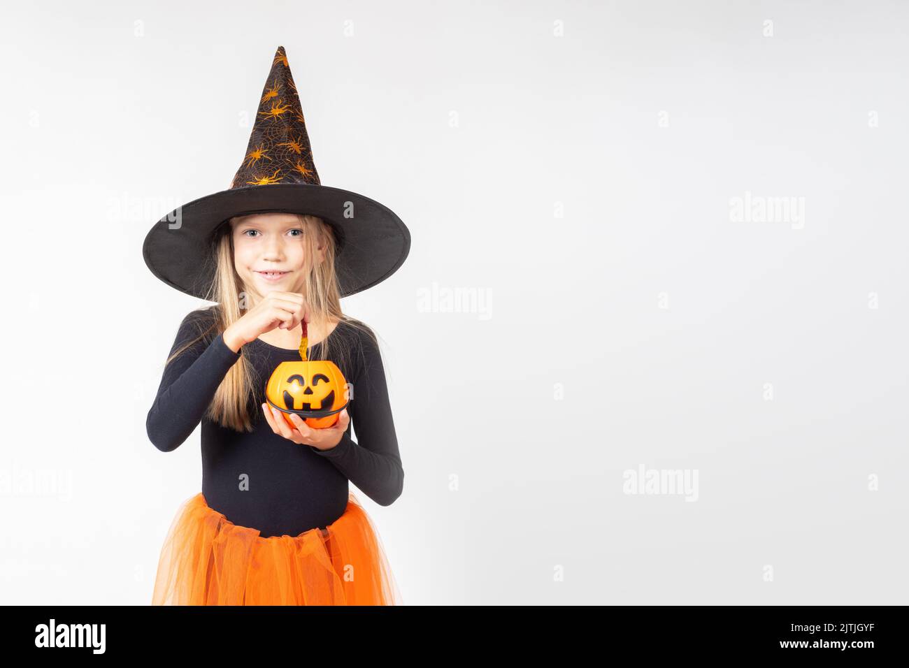 Kids Halloween. A beautiful cute girl in a witch costume, wearing a hat, takes out candy from a basket in the shape of Jack's lantern. Child having fu Stock Photo