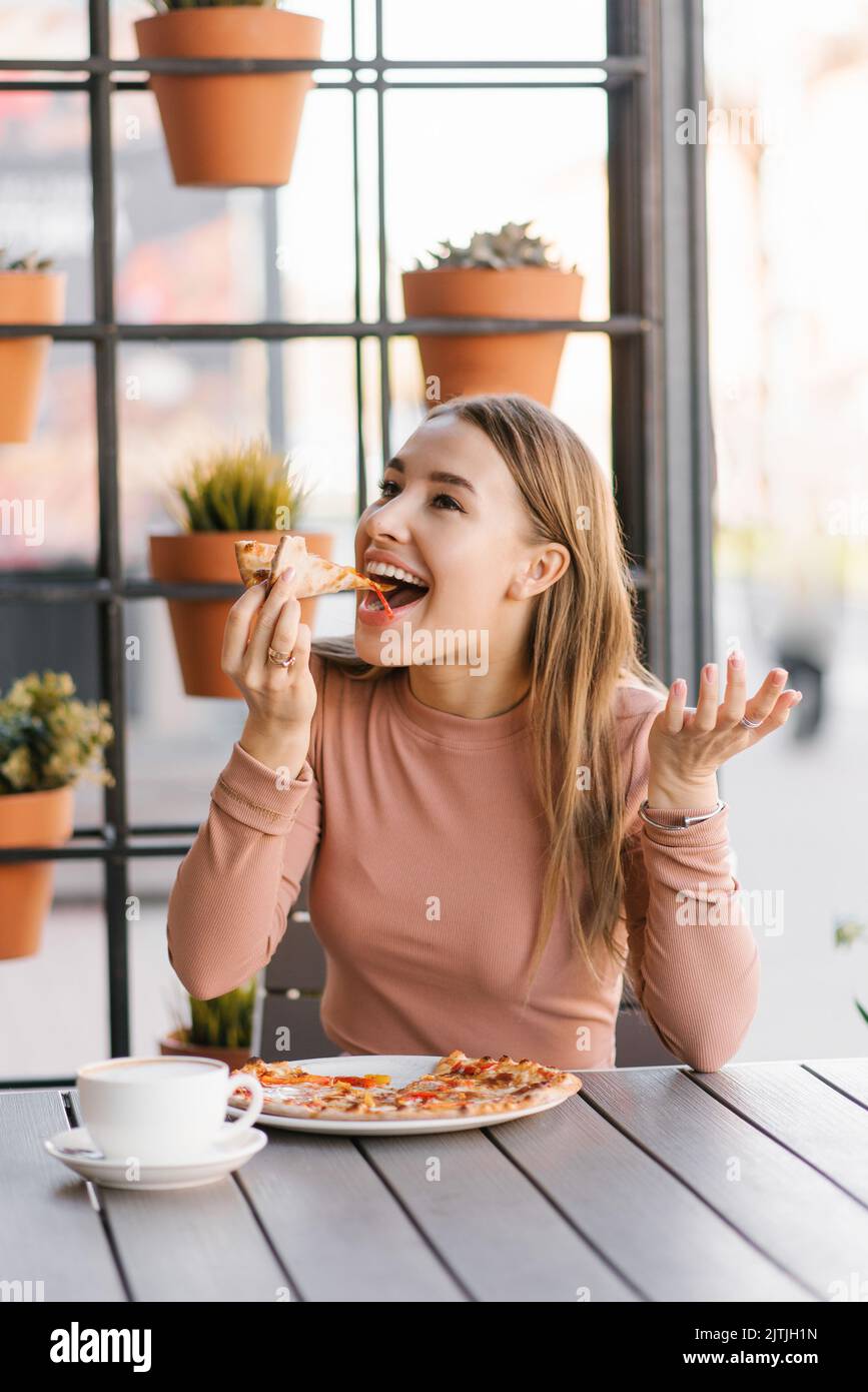 Funny European woman with a sweet smile eats pizza on the terrace of a summer cafe Stock Photo