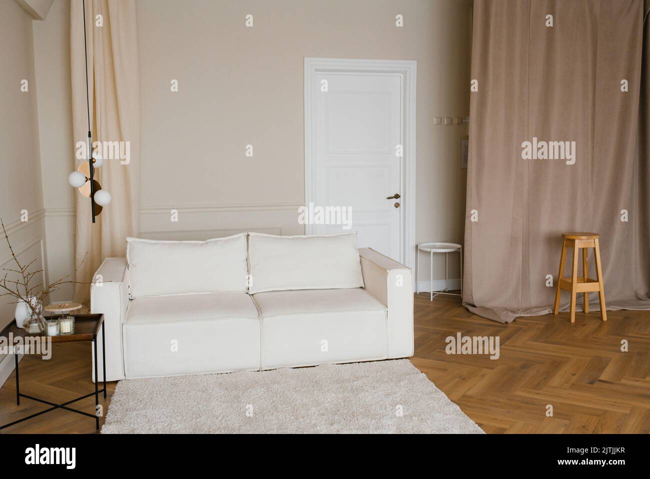 Scandinavian interior with a light sofa on a wooden parquet floor, a wooden side table and beige walls Stock Photo