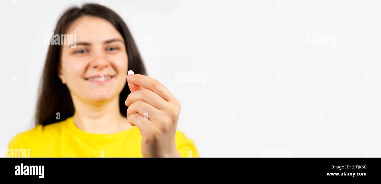 Beautiful healthy brunette woman holding a white pill on a white background with space for text. Stock Photo