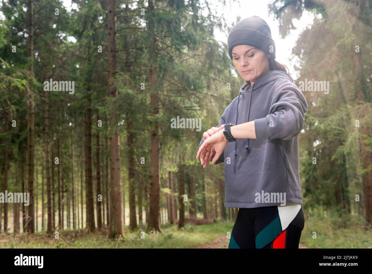 woman checking smartwatch tracker. Trail running runner girl looking at heart rate monitor smart watch in forest. Female athlete jogger training Stock Photo