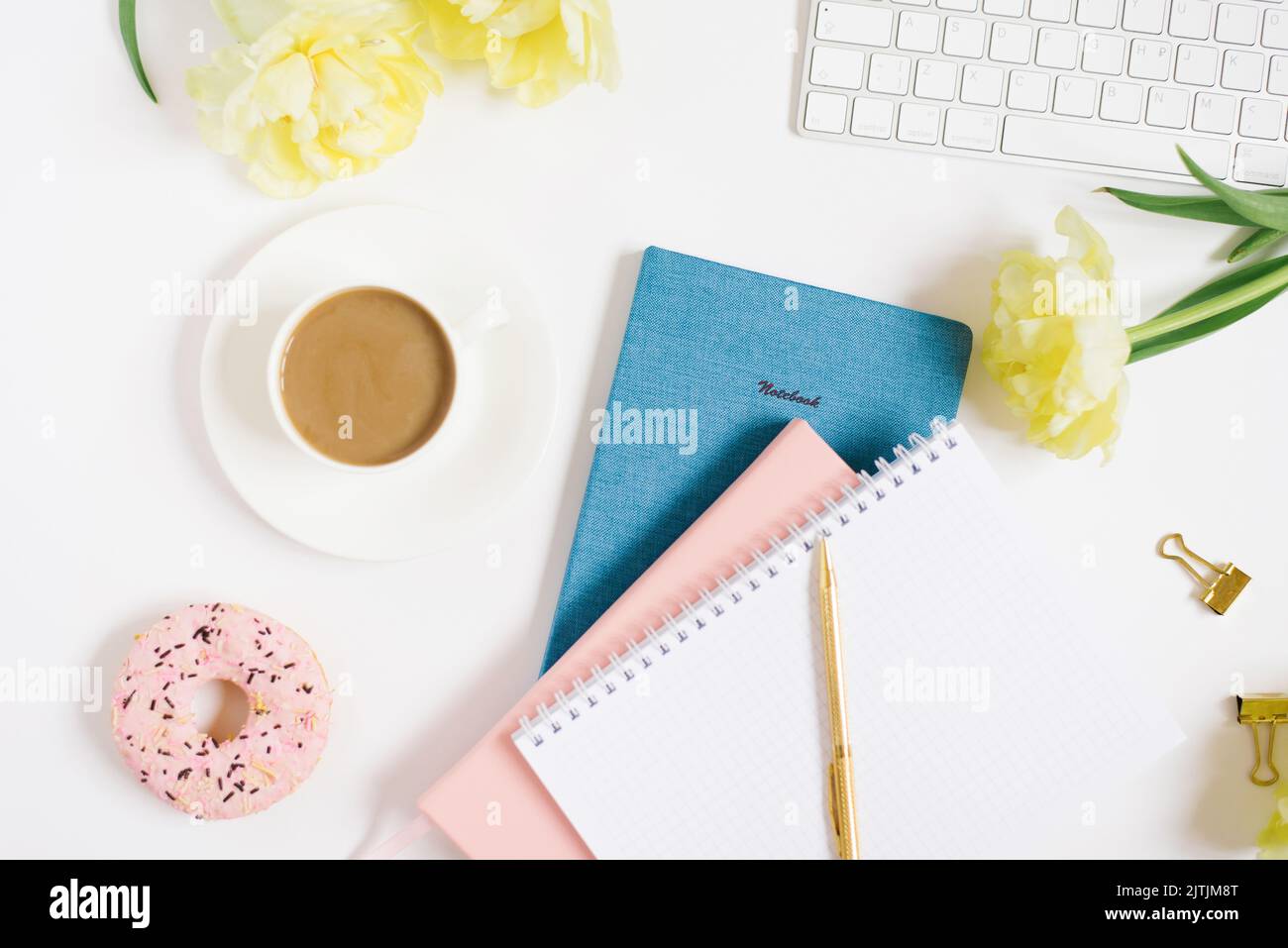 Notebook for daily planning with breakfast serving on a white background, a cup of coffee, a donut, flowers and a gift box with a bow. The concept of Stock Photo