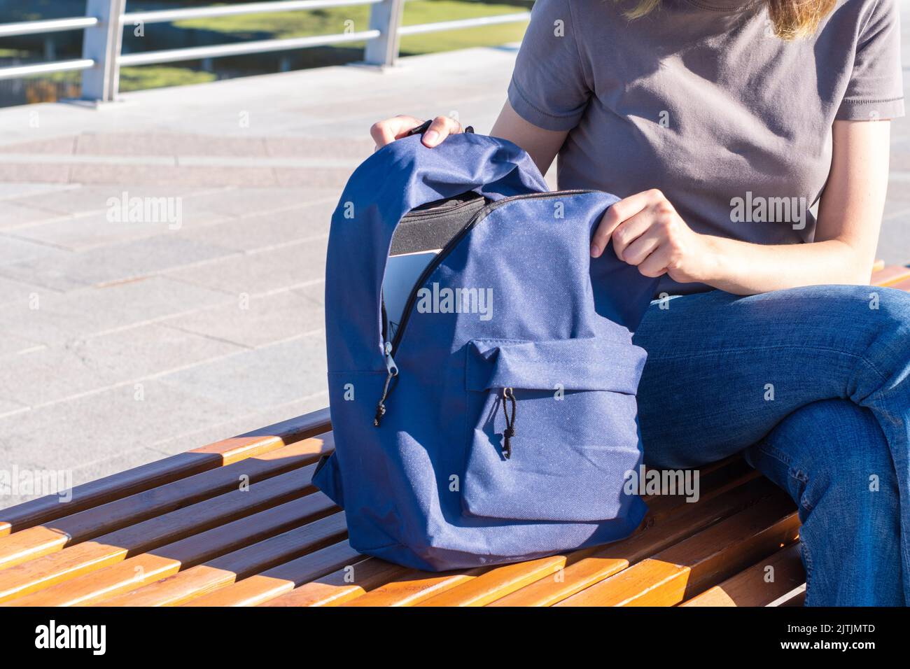 Women's hands zip up an orange school backpack with school supplies, books, an office, a laptop, on a park bench. The concept of Back to School. Stock Photo