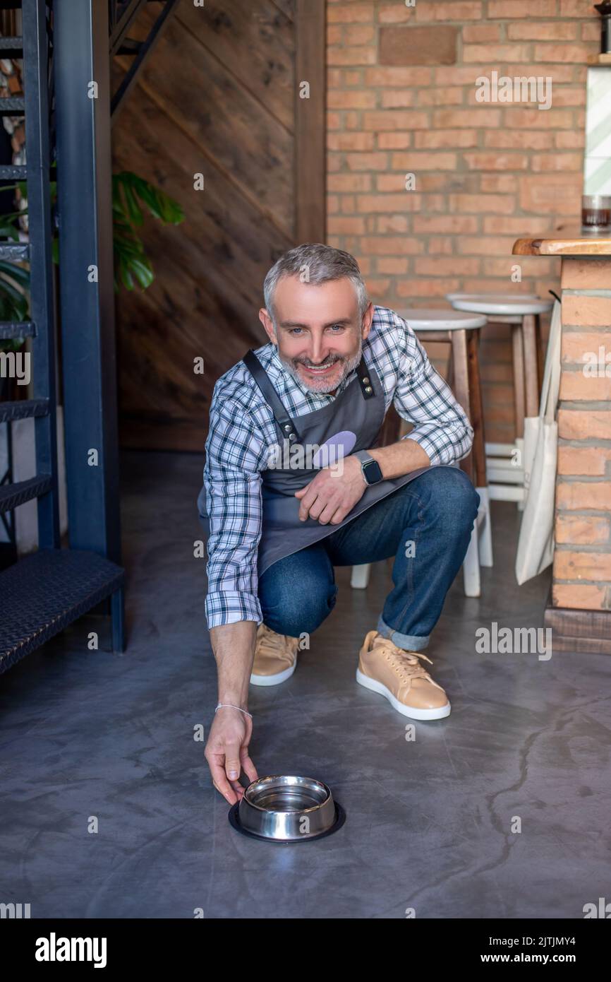 Kind-hearted coffee shop owner feeding a pet in his establishment Stock Photo