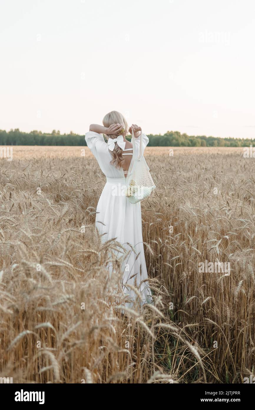 A blonde woman in a long white dress walks in a wheat field. The ...