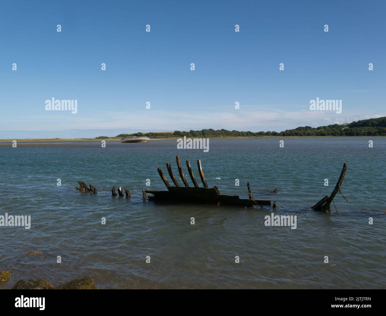 Remains of abandoned fishing boat with another one on sandbank Traeth Dulas estuary Anglesey North Wales UK in the background Stock Photo