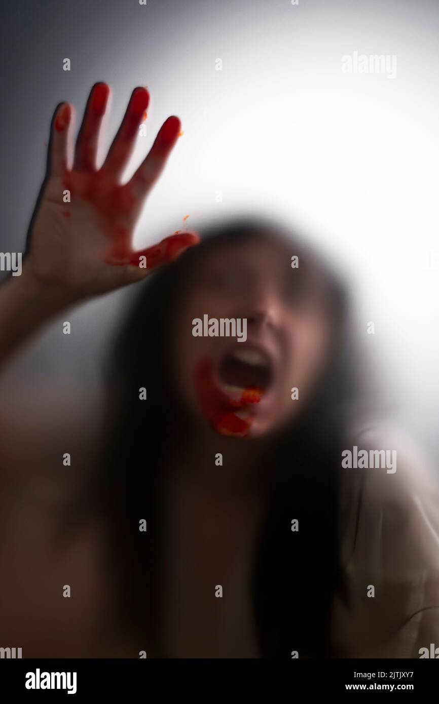 Horror ghost woman with blooded hands behind the matte glass. Halloween festival concept. Stock Photo