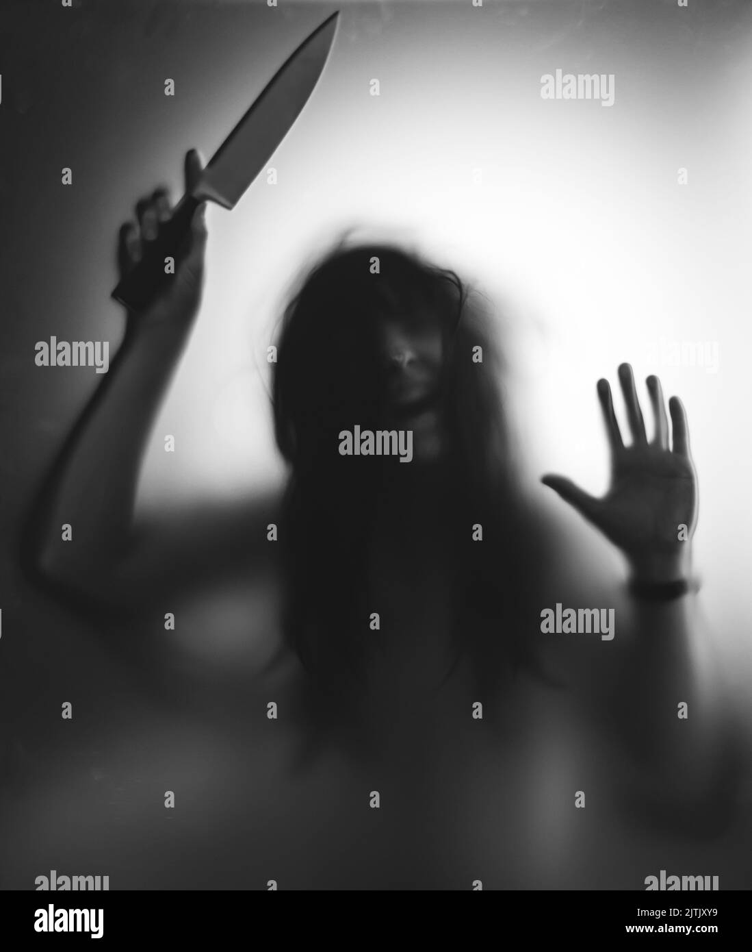 Horror, halloween background - Shadowy figure behind glass holding a knife Stock Photo