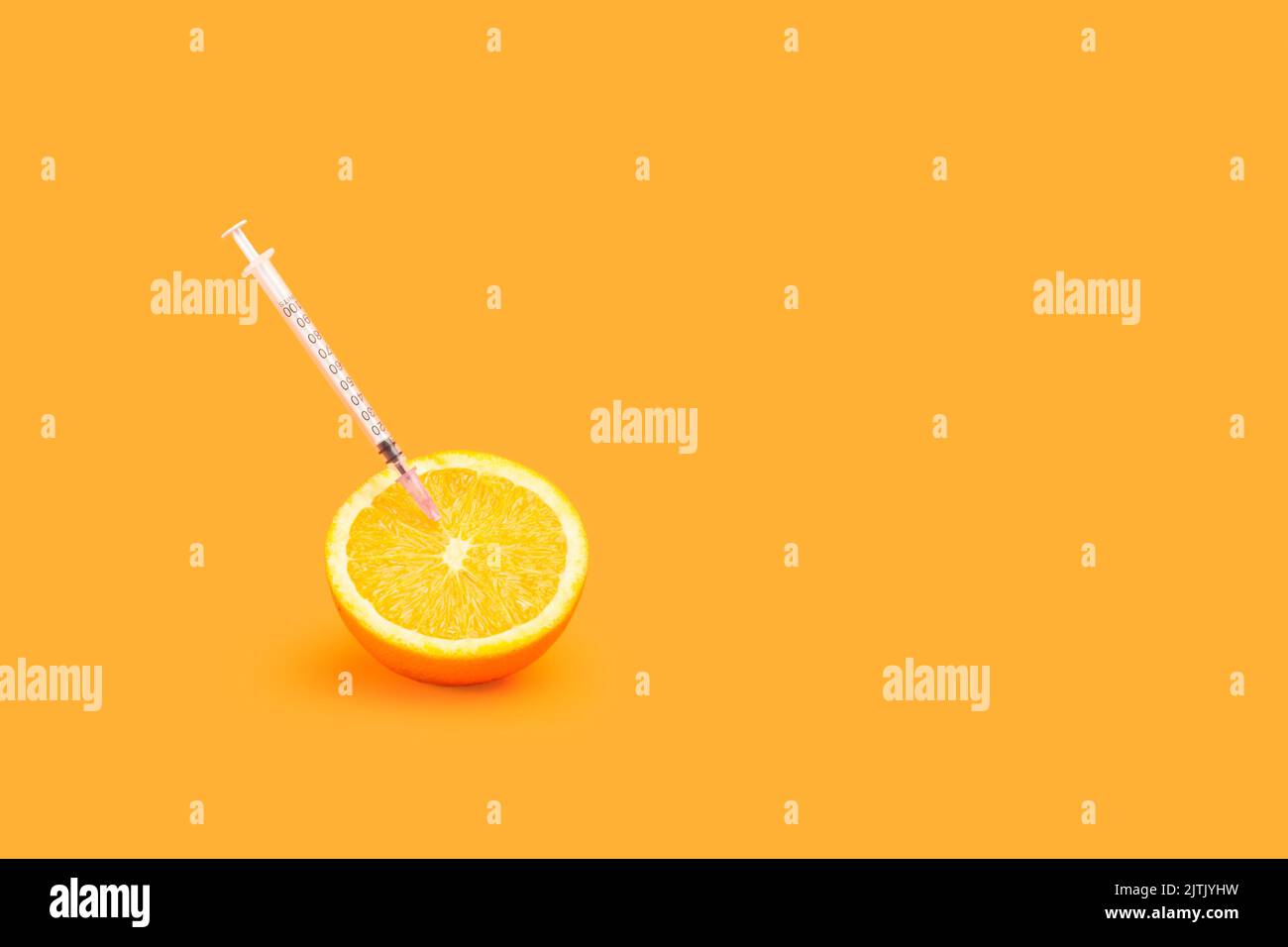 A half orange with a syringe stuck on an orange background with copy space Stock Photo