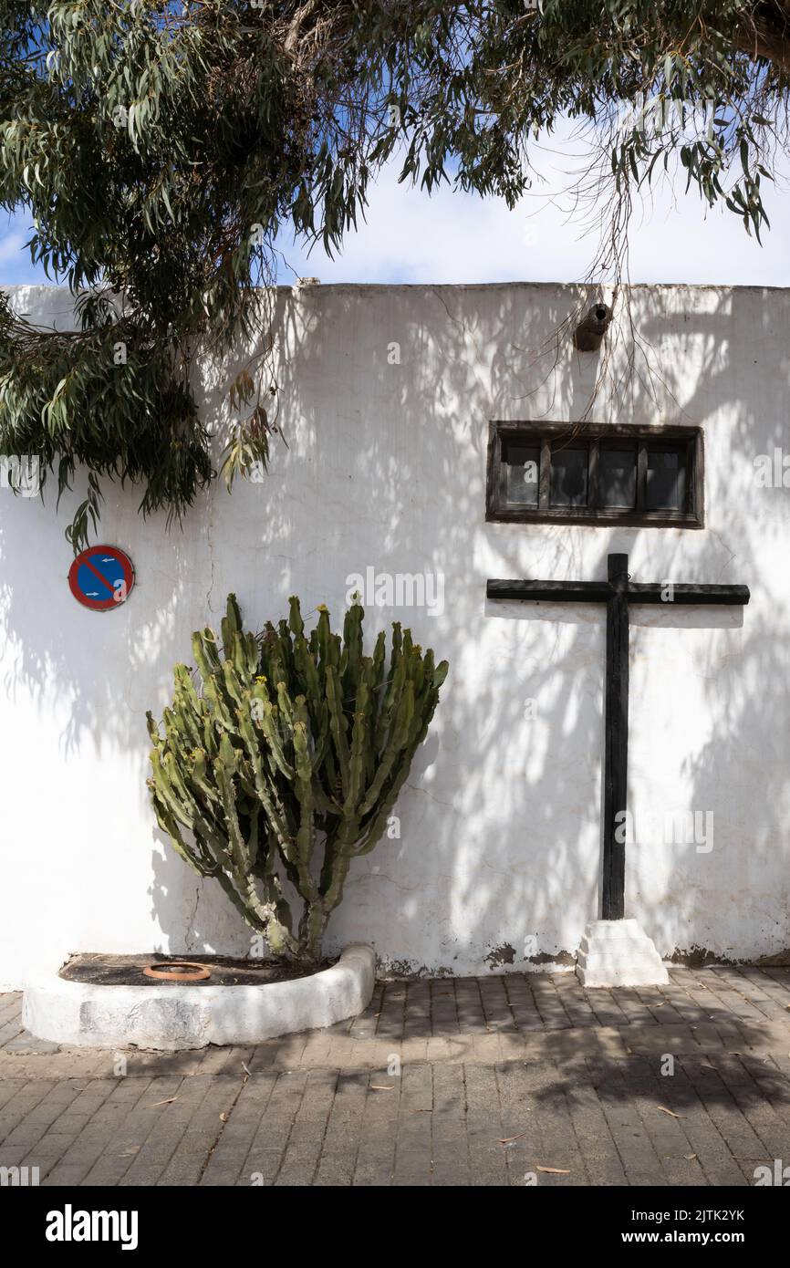 Romantic street with cactus plants and a wooden cross. White wall of the building. Leaves of a big tree above.. Traffic sign no standing. Teguise, Lan Stock Photo